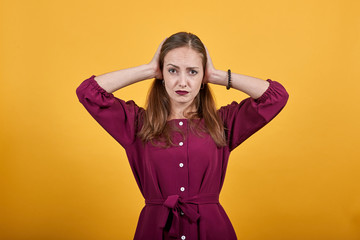 Young lady in burgundy bluse with bow over isolated orange background frustrated and covering ears