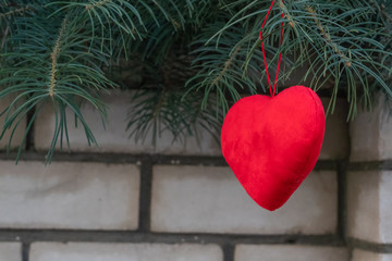 red heart hangs on a spruce tree on the street against a brick white wall. Copy space. concept of the outdoor festival.