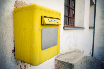 A bright old yellow post box on the wall, close up.
