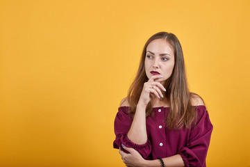 Ginger girl in burgundy bluse with bow over isolated orange background thoughtfully looks left and...