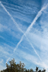 Fototapeta na wymiar Beautiful blue sky with X shaped airplane contrails and clouds.