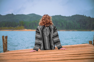 Young woman sitting on a pier watching a lagoon with mountains in the background and cloudy sky