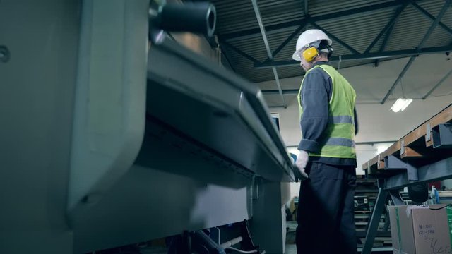 Plant worker is processing a metal sheet with a factory machine