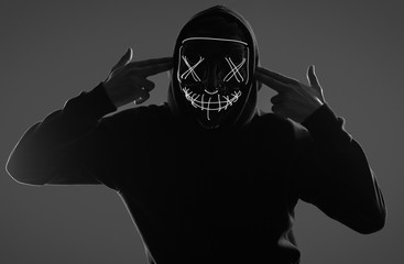 Anonymous man in black hoodie hiding his face behind a neon mask