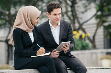 Young business couple in black suit  holding book and tablet sitting outside their office