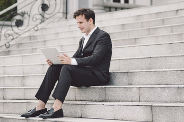 young handsome businessman with laptop relaxing on stairs, focus on laptop with smile face