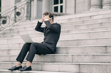 frustrated and depressed young business man sitting on stairs while working with his laptop