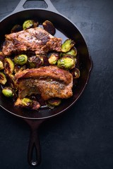 Vertical high angle shot of steak and grilled vegetables in a black pot on a black table