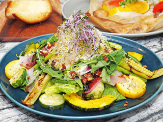 Warm salad with roasted vegetables with spices and sauce on a blue plate.