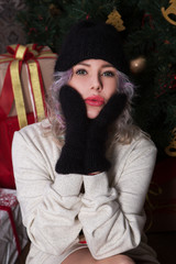 Beautiful happy woman in a knitted hat and mittens on the background of the Christmas tree.