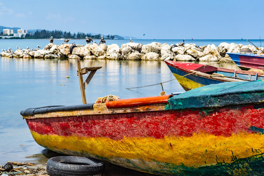 Colorful empty old wooden fishing boats docked by sea water in sand on shore. Coastal ocean view with birds on large rock boulders in background. Sunny summer tropical Caribbean island day outdoors.