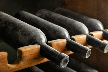 Wooden holder with bottles of wine in cellar, closeup