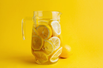 Jar full with lemon slices and fresh lemonade. Isolated on a bold, bright yellow background. Background and subject of the same color.