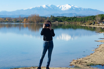Girl with curly hair takes pictures in a lake with the mountains in the background.Lake of Villeneuve-de-la-Raho (France) overlooking the Pyrenees and the Canigo. Concept: Landscape photography