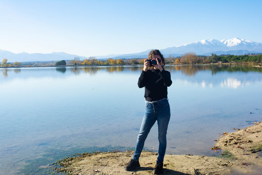 Girl with curly hair takes pictures in a lake with the mountains in the background.Lake of Villeneuve-de-la-Raho (France) overlooking the Pyrenees and the Canigo. Concept: Landscape photography