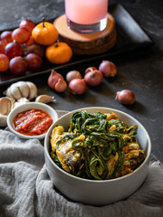 Ikan nila bumbu kuning and Cassava leaf vegetable is traditional food from indonesia served with strawberry syrup, grape, orange and onion and garlic garnish