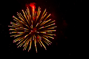 Yellow and red fireworks in the shape sphere on the left side on a black background.
