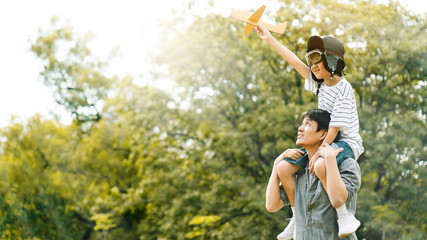 Asian family Father and son sat on his shoulders and run in the park. With paper plane as a toy in the hands of children And there are many big trees in the garden Is natural in the morning of summer