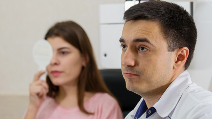 Ophthalmology treatment - young woman checking her visual acuity closing her eye with an eye shield - a doctor watching