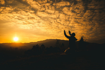 Pray of man kneeling down and lift hands at sunset background. christian silhouette concept. - obrazy, fototapety, plakaty