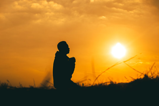 Man kneeling down and praying at sunset background. christian silhouette concept.