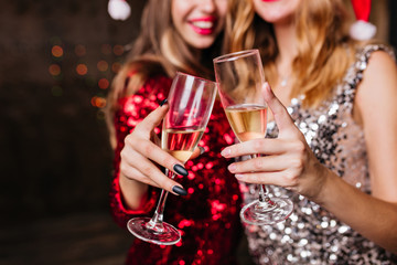 Cute ladies drinking champagne with pleasure in new year. European women in dresses celebrating winter holidays with wine.