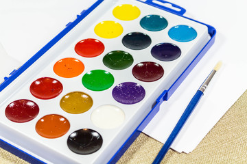 A new box with multi-colored paints and a brush for painting. Diagonally