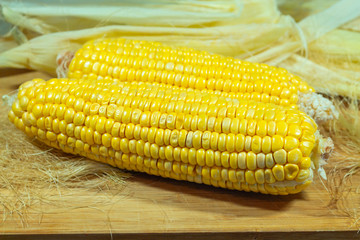 Patch of corn peeled on a wooden board on a background of leaves. Two pieces