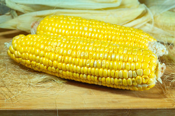 Patch of corn peeled on a wooden board on a background of leaves. Two pieces