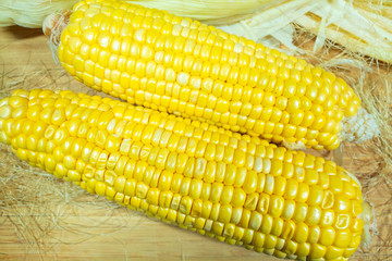 Patch of corn peeled on a wooden board on a background of leaves. Two pieces