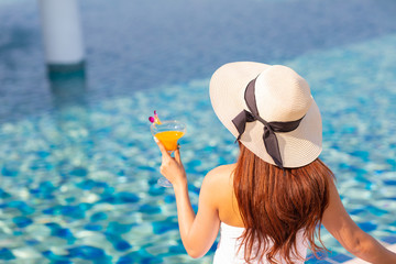 Portrait of a beautiful woman relaxing with orange juice at the swimming pool outdoors
