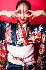 young pretty geisha on red background posing in kimono, oriental concept