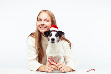 pretty young blond girl with her little cute dog wearing Santas red hat at Christmas holiday isolated on white background, lifestyle people concept