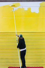 Painting a wall yellow with a long roller brush