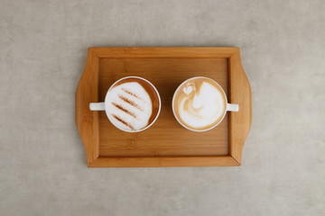 Tow cappuccino and mocha cups served on wooden tray on white texture background