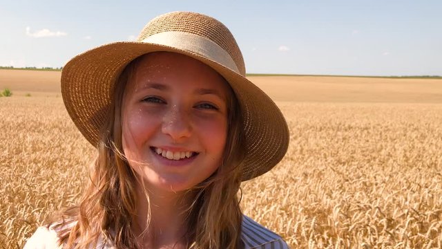 Face emotions. Teenager girl in a straw hat on a background of a wheat field smiling.