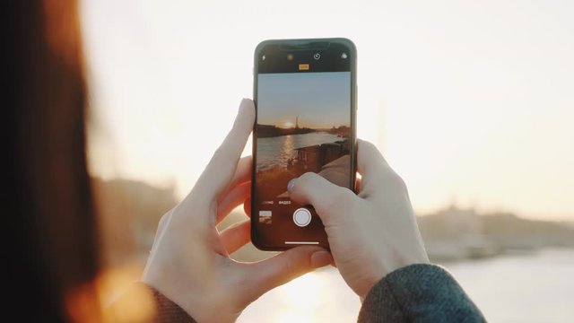 Cinematic close-up, happy woman taking smartphone photo of sunset over Eiffel Tower and Seine river in Paris slow motion
