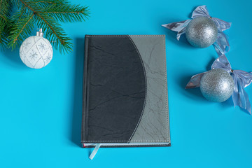 Gray notebook surrounded by silver glittering Christmas decorations on a blue background, top view..