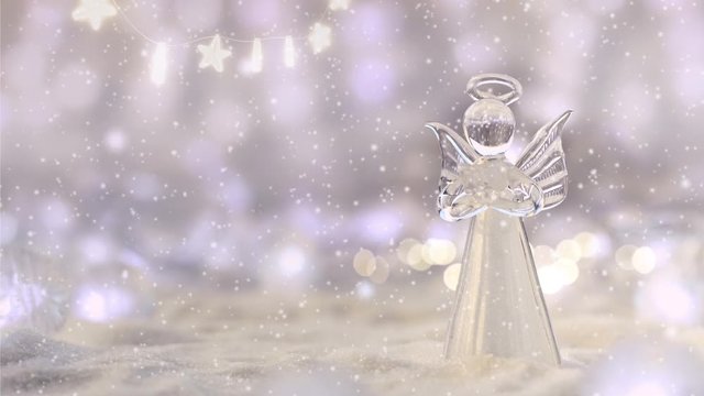 Merry Christmas & Happy New Year greeting card with snow falling and copy space for your text. Little angel in the white glitter bokeh background. 