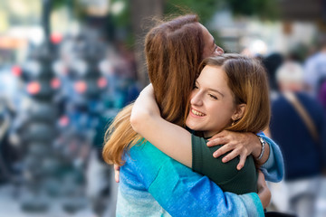 Happy teenage girl hugging her mother on the street, outdoors.