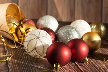 Christmas gifts, gold, silver, red Christmas balls spilled out from a package of kraft paper on a wooden background. Christmas balls. Copyspace.