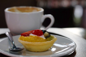 Mix fruit tart on white dish and hot coffee served on wood trey in a restaurant, famous refreshment...