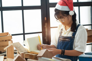 Asian teen in a Santa hat works in her woodwork in workshop, Christmas time