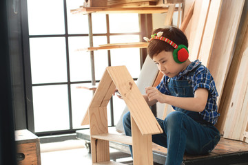 Asian boy with his woodwork in carpentry workshop studio, Christmas earmuffs at ears of boys