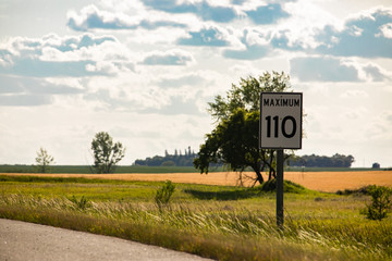 110 km maximum speed limit sign on the roadside against yellow prairies and plains view on the...