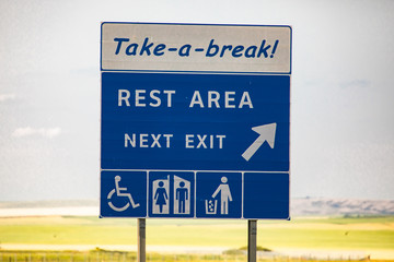 take a break, Rest area in the next exit, Tidy man, toilets, Special needs symbols., Information Road blue Sign against yellow prairies and plains