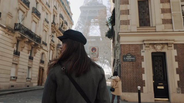 Camera follows happy beautiful smiling tourist woman towards Eiffel Tower square on romantic Paris vacation slow motion.