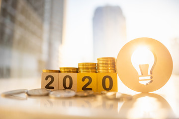 Wooden number 2020 with stack of coins , lamp idea on blurred city scape and copy space for text using as background business investment, new year concept.