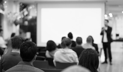 Fototapeta premium Speaker giving a talk at a corporate business conference. Audience in hall with presenter in front of presentation screen. Corporate executive giving speech during business and entrepreneur seminar. 