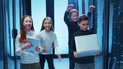 Cute cheerful school kids celebrating dancing together in data center. Young adorable team of teenagers having fun exciting time inside database cyber security. - Powered by Adobe